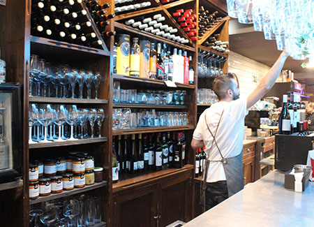 Vista del interior del bar, dónde podemos ver lo que hay detrás de la barra, múltiples botellas de vino y de licor,muchos tipos de copas y botes de conservas artesanales