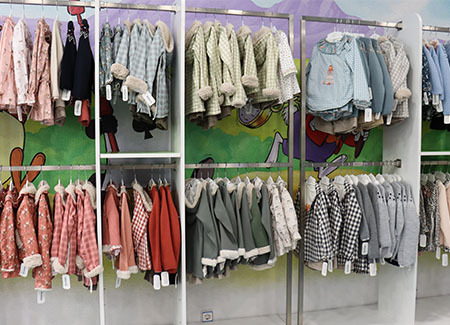 Vista del interior del comercio, dónde podemos ver muchas prendas de ropa expuestas en un perchero tipo burro de dos niveles y con separadores entre las prendas de diferentes colores