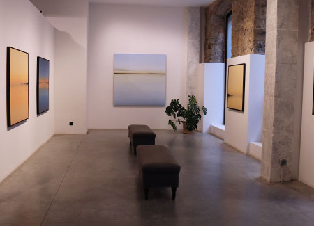 Vista del interior de la galería, dónde podemos ver cuatro cuadros dispuestos en tres paredes, con dos bancos situados en el medio de la misma
