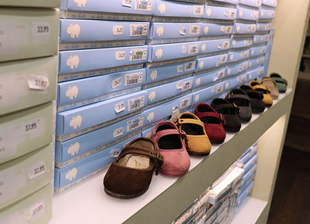 Primer plano de una estantería dónde vemos las cajas de los diferentes productos, con un hilera de zapatos infantiles de diferentes colores por delante de las cajas