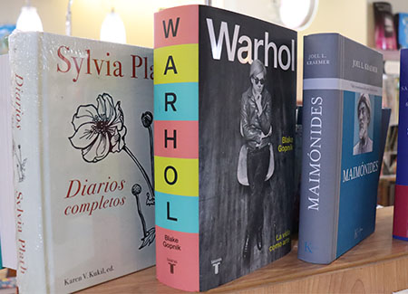 Primer plano de tres libros en un expositor: Diarios completos, de Sylvia Plath, Warhol y Maimónides
