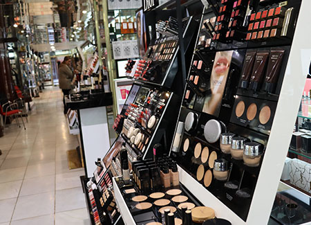 Vista del interior del comercio, dónde vemos, en primer plano, un expositor de maquillaje, al fondo se ve uno de los pasillos con productos de la perfumería