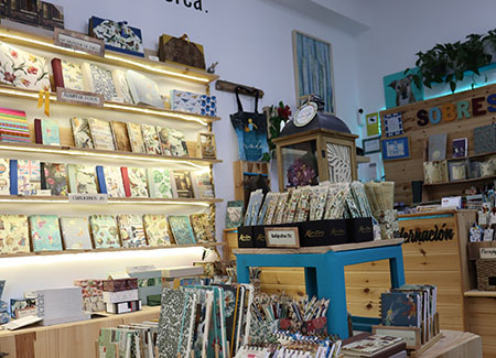 Vista de una parte de la tienda donde podemos ver un expositor con libretas artesanales contra la pared y otras sobre una mesa en primer plano