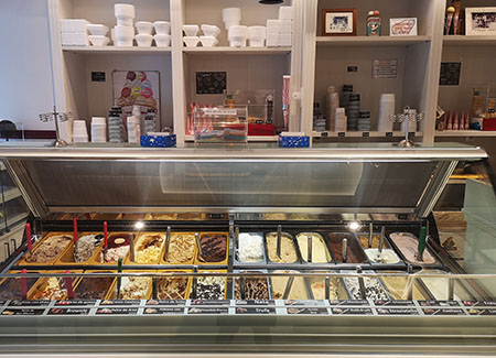 La vitrina grande de helados, con 24 sabores, de fondo las estanterías donde están los recipientes, cucuruchos y otros elementos