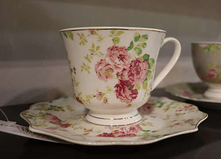 Primer plano de una taza de café de cerámica sobre un plato del mismo material. Ambos elementos están decorados con motivos florales de rosas
