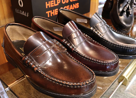 Primer plano de un par de zapatos marrones sin cordones para hombre. A su lado un zapato suelto del mismo modelo pero en color negro