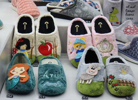 Primer plano de cuatro pares de zapatillas infantiles con motivos de princesas y animales