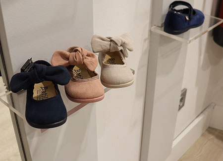 Primer plano de un estante de metacrilato con tres zapatos de bebé con un lazo, cada uno de un color diferente