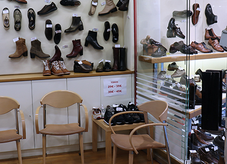 Vista del interior del comercio, dónde se pueden ver zapatos y botas presentados en expositores y en una pared, así como sillas para los clientes