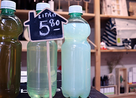 Primer plano de tres botellas de plástico rellenas de líquidos de diferentes colores con un cartel de pizarra con el precio: Litro 5,80
