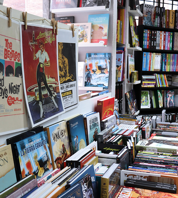 Vista del interior de la librería, dónde podemos ver una amplia selección de cómics en un expositor y un librería, junto a carteles de tipo retro colgados de una cuerda