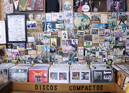 Vista del interior del comercio, dónde vemos un expositor de discos de vinilo, en la pared de detrás podemos ver fotos, postales y carteles antiguos.