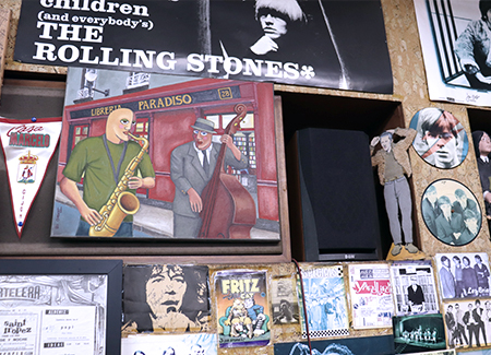 Primer plano de una pared en la que se pueden ver carteles, portadas de discos y un cuadro que muestra a dos músicos frente a la librería