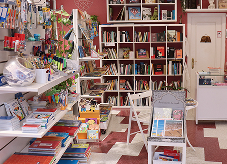 Vista del interior de la tienda, dónde podemos ver a la izquierda unas baldas con material de papelería, a su lado un expositor con baldas llenas de libros y al fondo una estantería con más libros