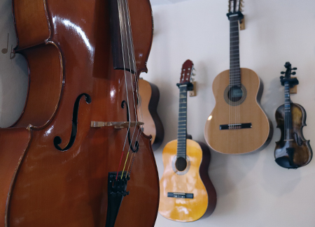 Primer plano del cuerpo de un violín de madera rojiza, al fondo, colgados en un pared se ven otro violín junto a tres guitarras españolas