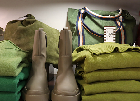 Primer plano de una balda donde vemos prendas de ropa, bolsos y botines de tonos verdosos