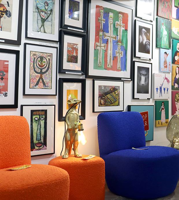 Vista del interior del comercio, dónde podemos ver una pared cubierta de cuadros, dos sillones, uno azul y el otro naranja, con un taburete naranja entre ambos que tiene encima una lámpara con forma de ratón